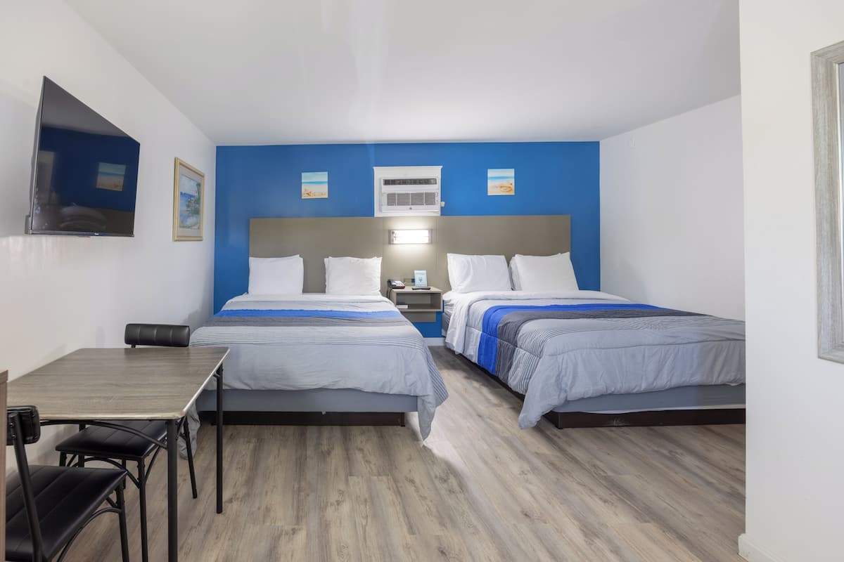 Une chambre d’hôtel avec deux lits, un bureau, une chaise, une télévision et un appareil de climatisation.