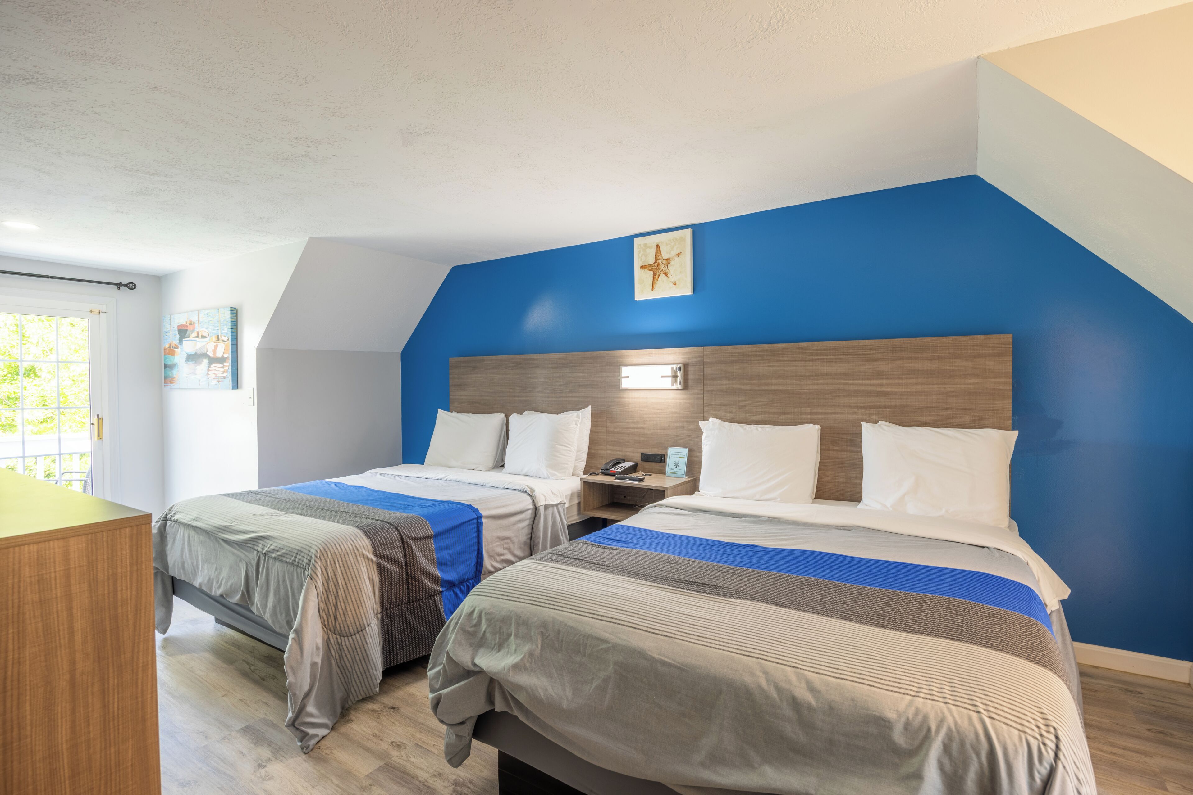 A hotel room with two beds, a wooden headboard, a star decoration, and a window with a view.