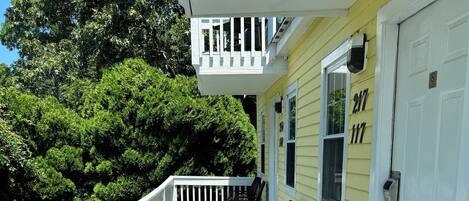 A covered porch with a railing, two chairs, and a door with the number 217.