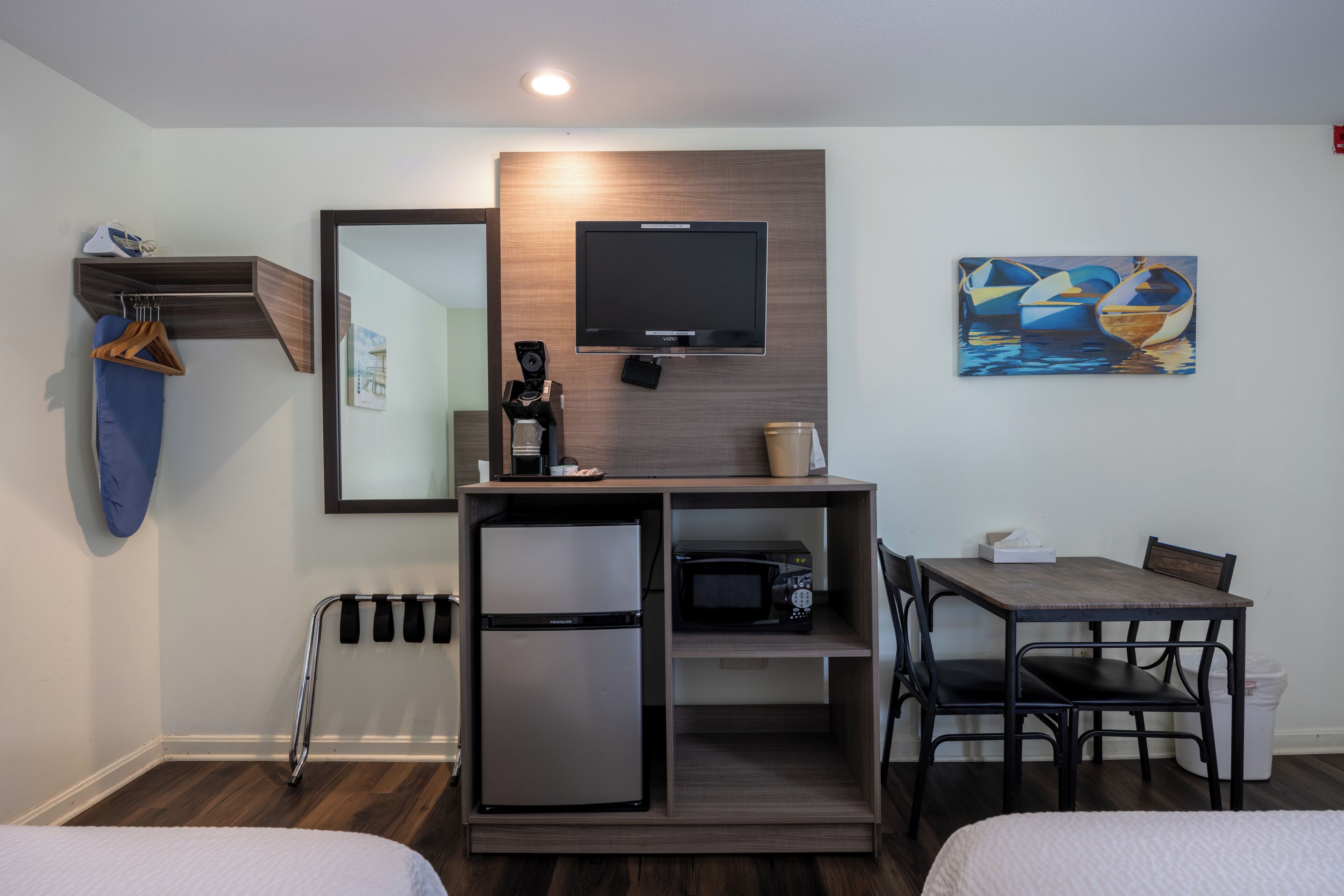 Une chambre d’hôtel comprenant un lit, un bureau avec une chaise, un four à micro-ondes, un réfrigérateur, une télévision et un tableau au mur.