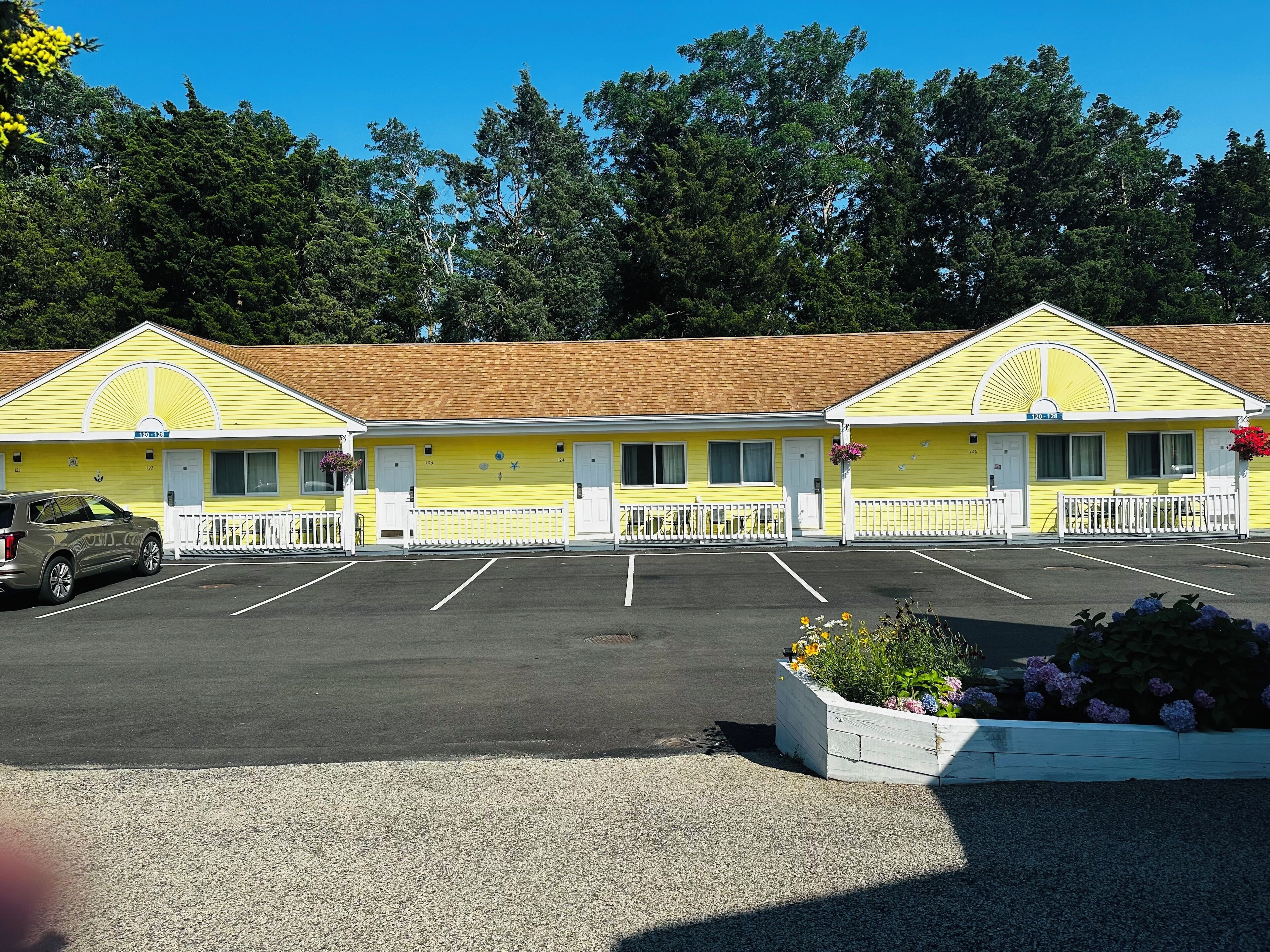 A motel with three yellow buildings, a parking lot, and a flower bed.