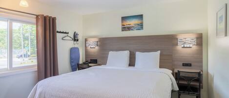 A hotel room with a large bed, bedside tables, a chair, a window with curtains, and a painting on the wall.