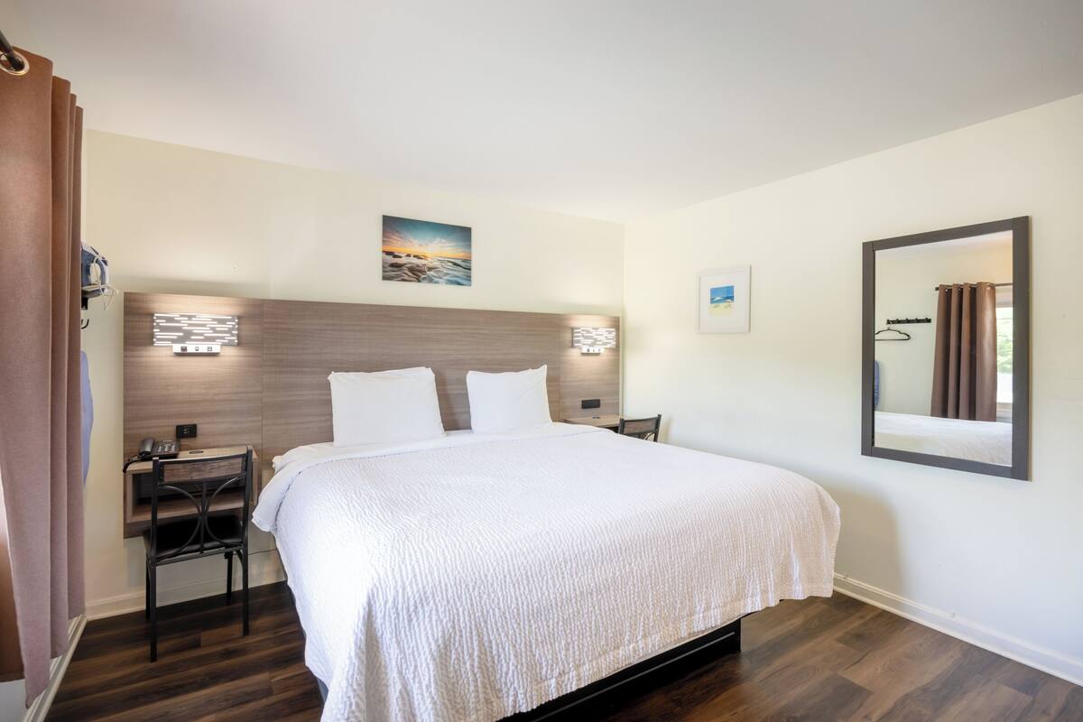 Une chambre d’hôtel comprenant un lit, des tables de chevet, un bureau, une chaise, un miroir et une œuvre d’art accrochée au mur.