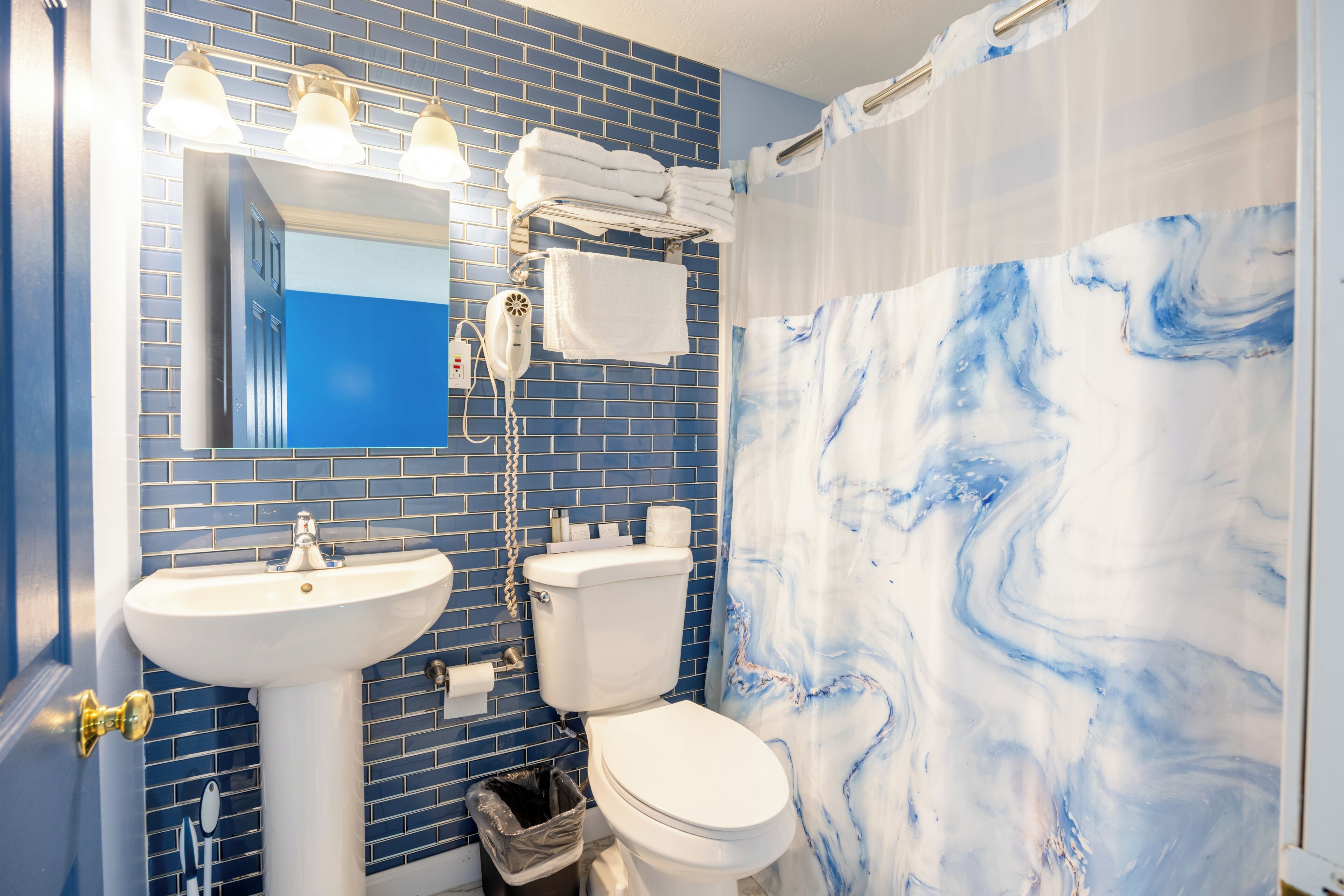 A bathroom with a blue tiled wall, a white sink, a toilet, and a shower curtain with a marble pattern.