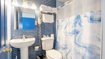 A bathroom with a blue tiled wall, a white sink, a toilet, and a shower curtain with a marble pattern.