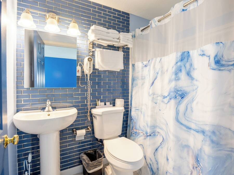 A bathroom with a blue tiled wall, a white sink, a toilet, and a shower curtain with a marble pattern.
