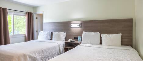 Habitación de hotel con dos camas, una mesita de noche, un teléfono y una ventana con cortinas.