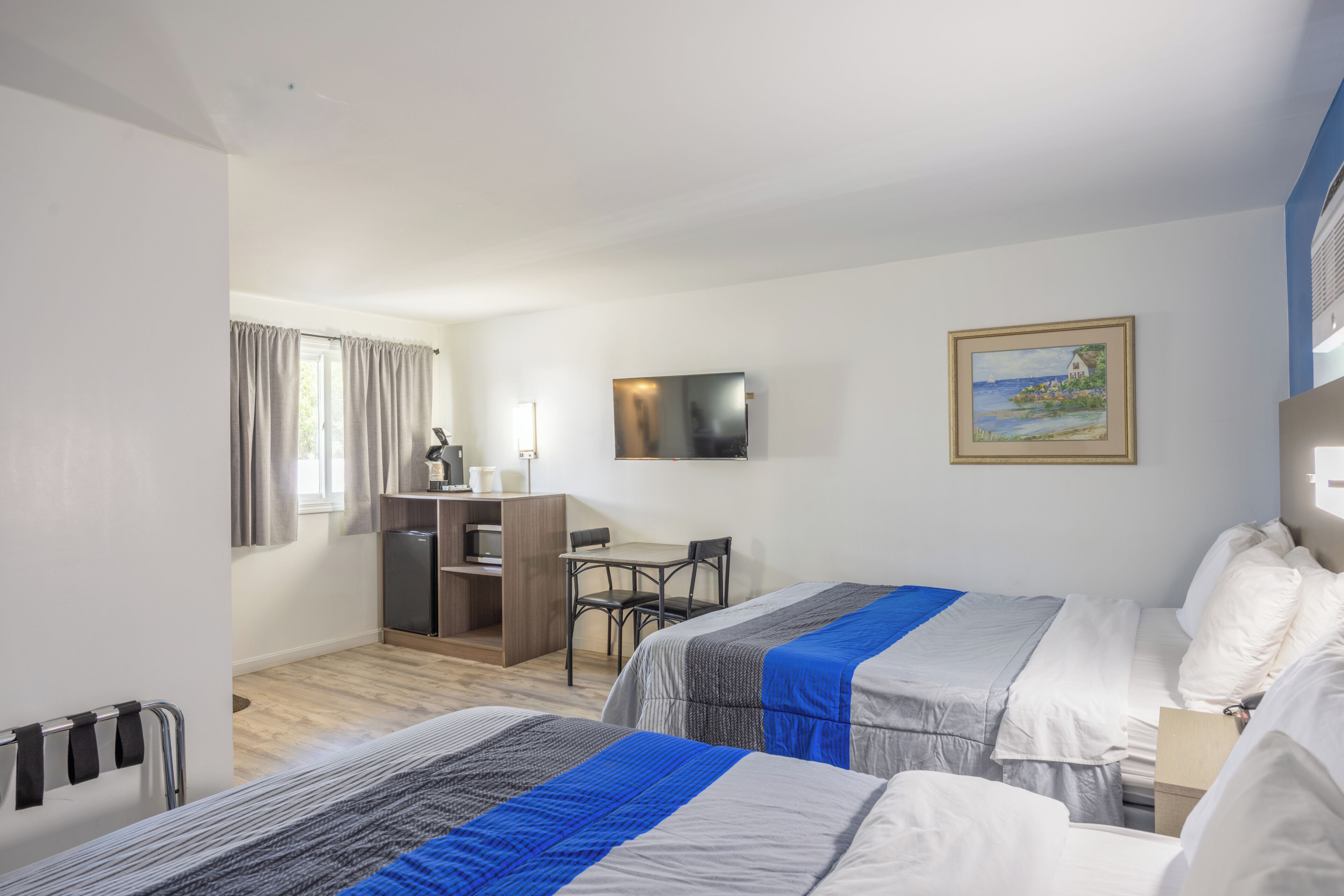 Quarto de hotel com duas camas, uma escrivaninha, uma televisão e um quadro na parede.