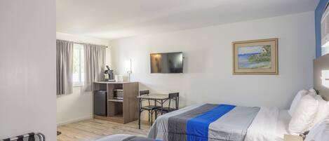 A hotel room with two beds, a desk, a television, and a painting on the wall.