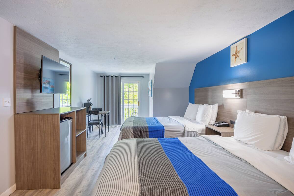 Ein Hotelzimmer mit zwei Betten, einem Schreibtisch, einem Kühlschrank und einem großen Fenster.