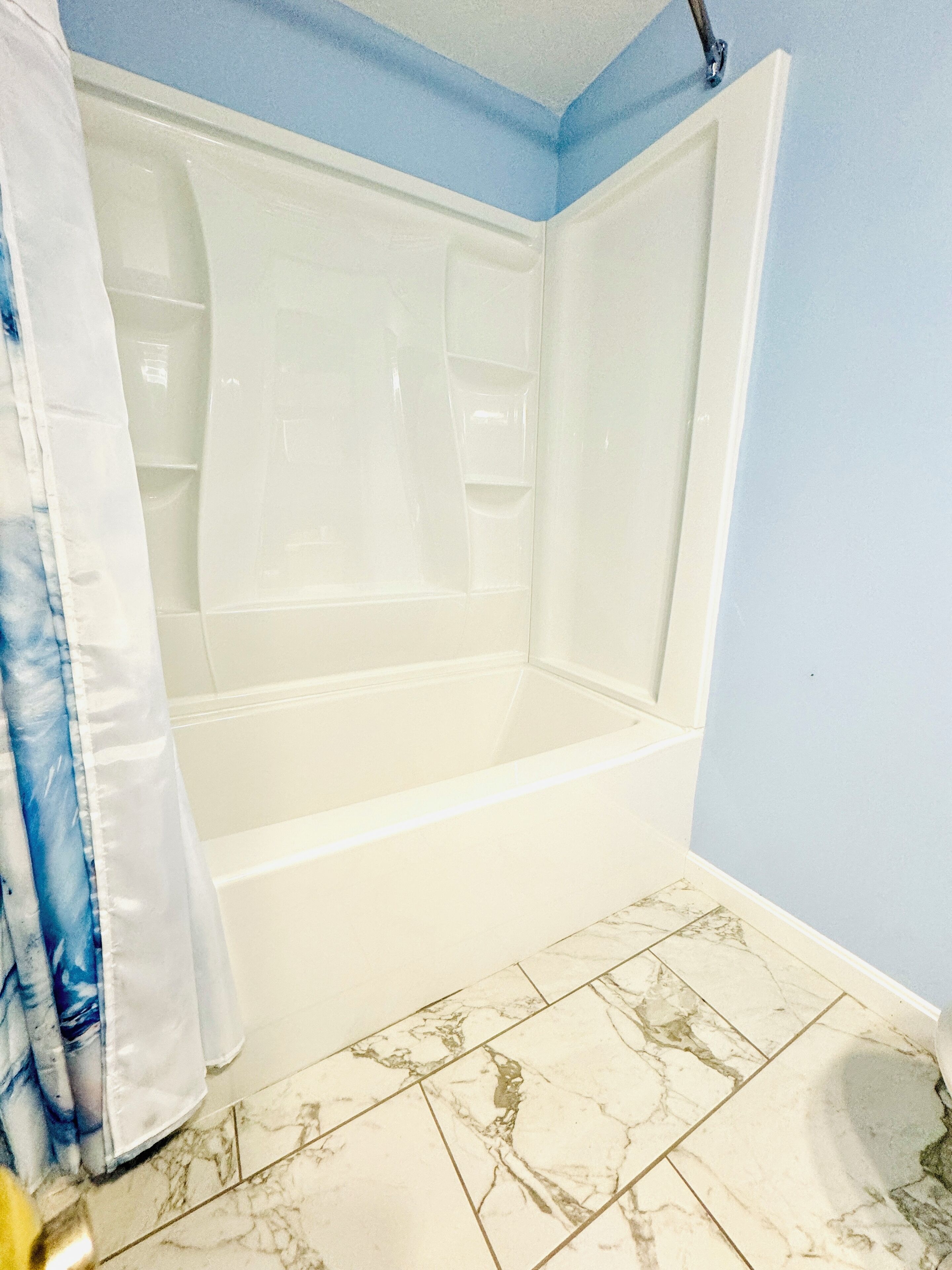 Un baño con bañera, cortina de ducha y baldosas de mármol.