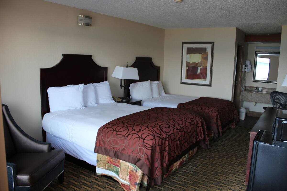 A hotel room with two beds, a desk, a chair, a lamp, and a painting on the wall.