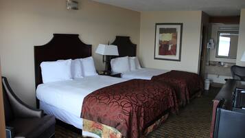 A hotel room with two beds, a desk, a chair, a lamp, and a painting on the wall.