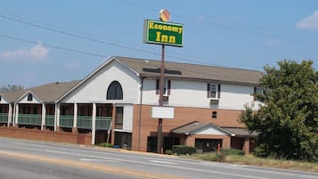 Een Economy Inn met twee verdiepingen, met een opvallend groen en geel bord, een gevel van baksteen en een overdekte veranda.