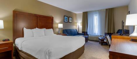 Una habitación de hotel con una cama grande, un escritorio, una silla, una lámpara y una ventana con cortinas.