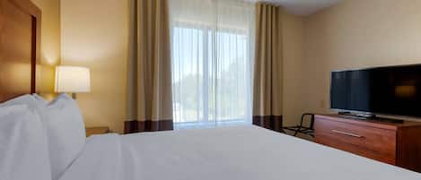 Una habitación de hotel con cama, televisión, lámpara y ventana con cortinas.