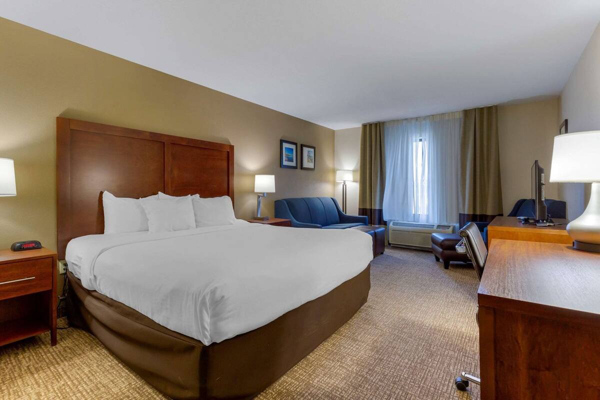 Ein Hotelzimmer mit einem großen Bett, einem Schreibtisch, einem Sessel, einem Fernseher und einem Fenster mit Vorhängen.