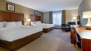 A hotel room with two beds, a desk, a chair, a TV, and a window with curtains.