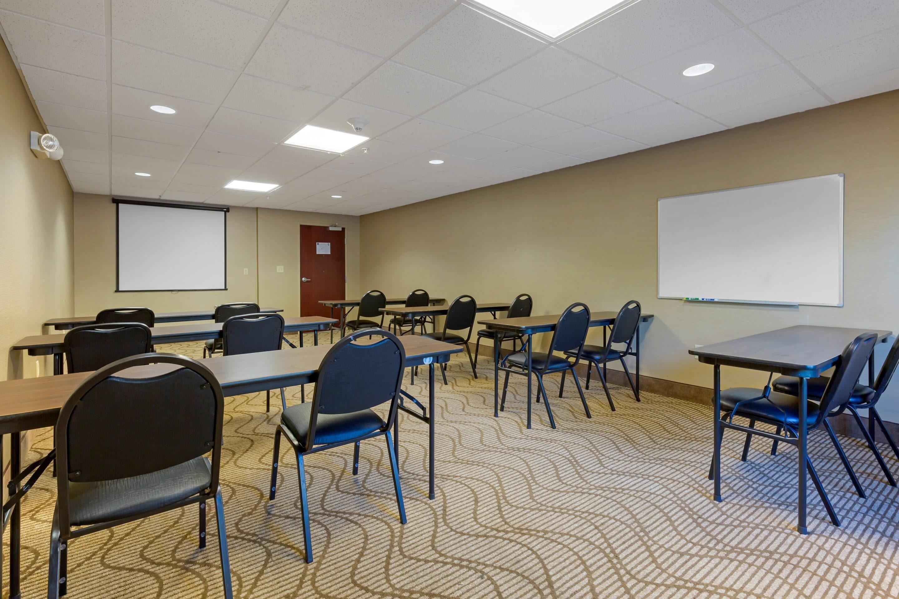 A conference room with tables and chairs, a projector screen, and a whiteboard.
