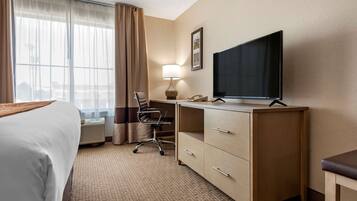 Una habitación de hotel con cama, escritorio, silla, televisión y un ventanal con cortinas.