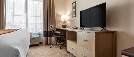 A hotel room with a bed, desk, chair, TV, and a large window with curtains.