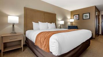 A hotel room with a large bed, two bedside tables with lamps, a wooden headboard, and a carpeted floor.