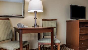 A hotel room with a wooden desk, two upholstered chairs, a telephone, a lamp, a television, and a cabinet.