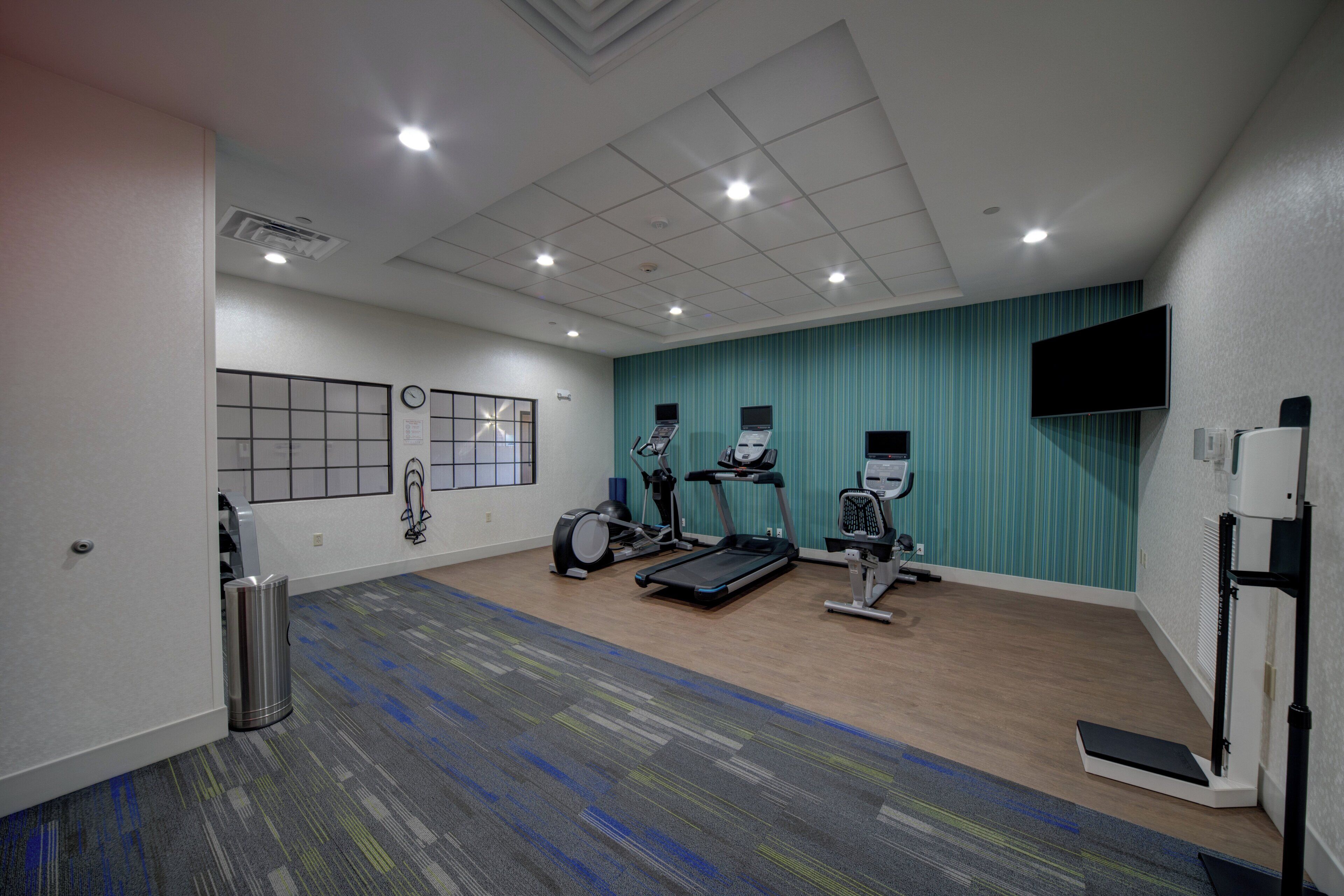 A gym with exercise equipment, a clock, and a TV on the wall.