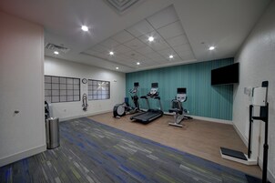 Un gimnasio con equipo de ejercicio, un reloj y un televisor en la pared.