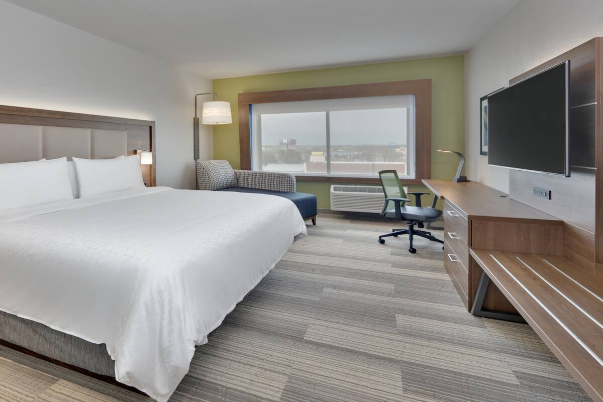 A hotel room with a large bed, a desk with a chair, a TV, and a window with a view of the city.
