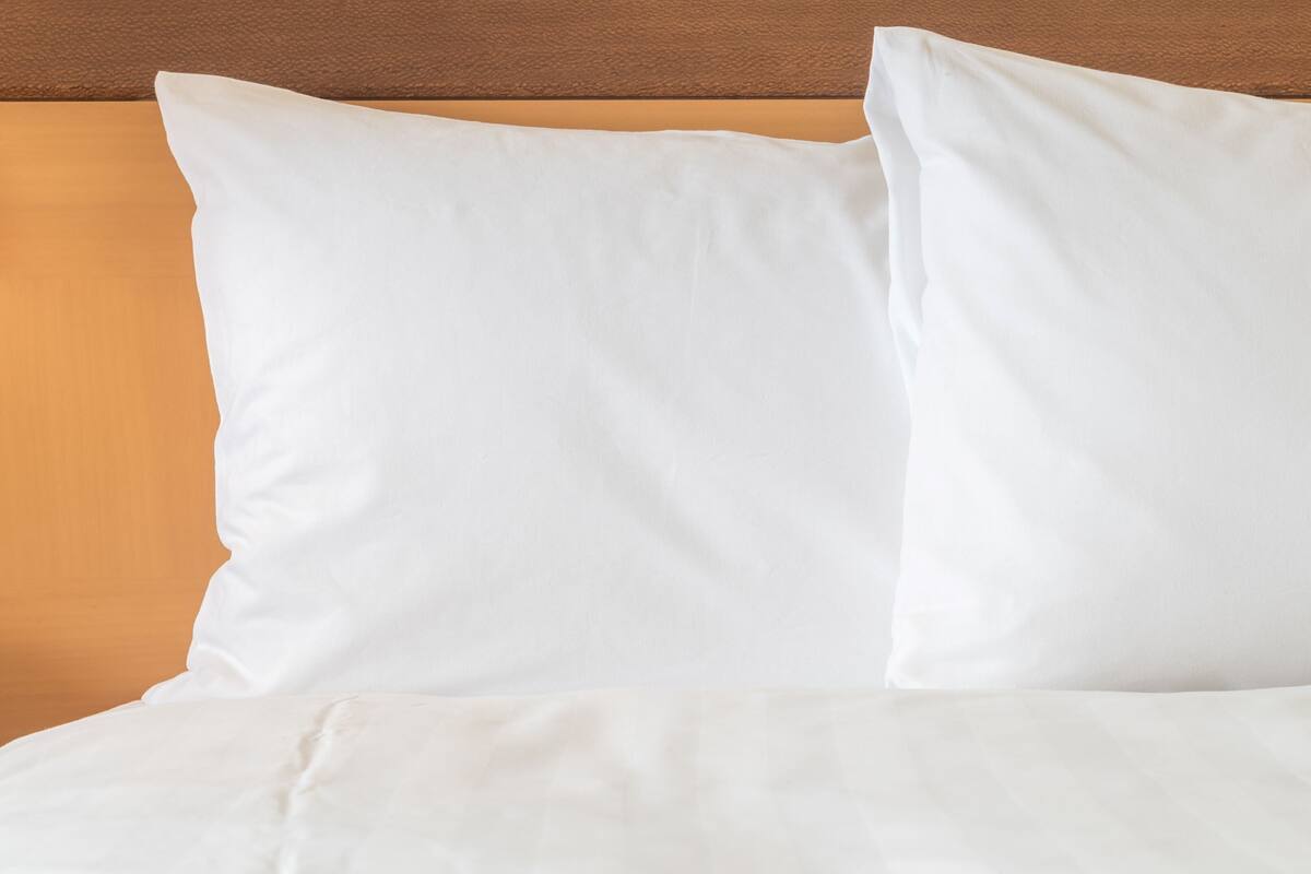 A bed with white bedding and pillows against a wooden headboard.