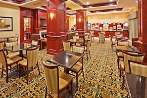 A hotel lobby with multiple dining tables and chairs, a patterned carpet, and wooden decor. - Holiday Inn Express & Suites Oklahoma City West-Yukon by IHG (Yukon)