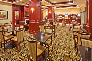 Un vestíbulo de hotel con varias mesas y sillas para comer, una alfombra estampada y detalles de madera.