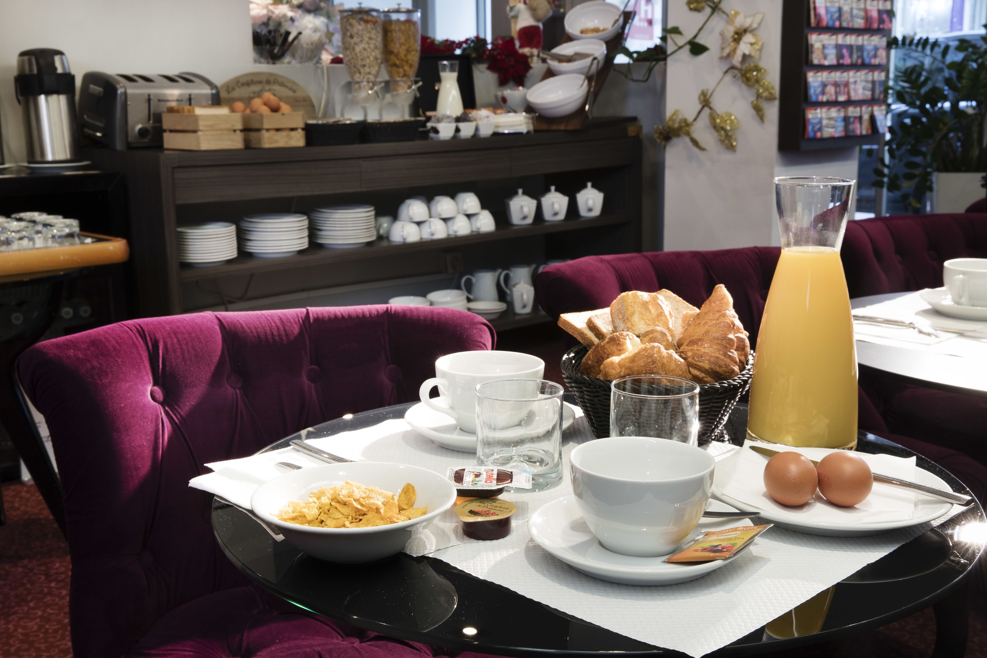 A breakfast setting with a table set for two, including plates, bowls, cups, and a juice pitcher.