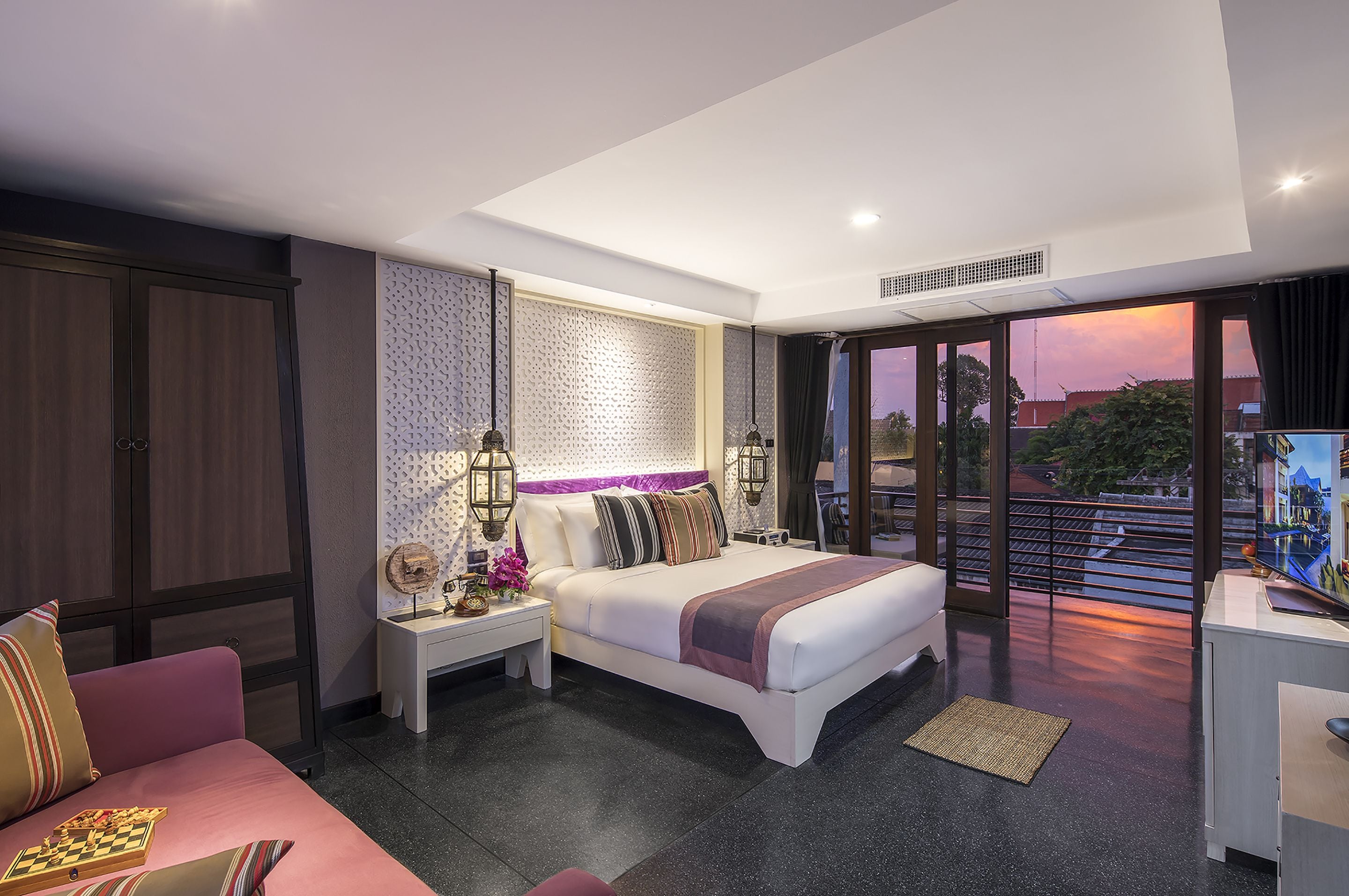 A modern hotel room with a large bed, a sofa, a desk, and a balcony with a city view.