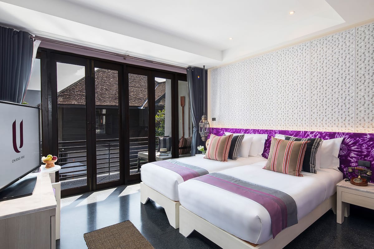 A hotel room with two beds, a desk, and a large window with a view of the outside.