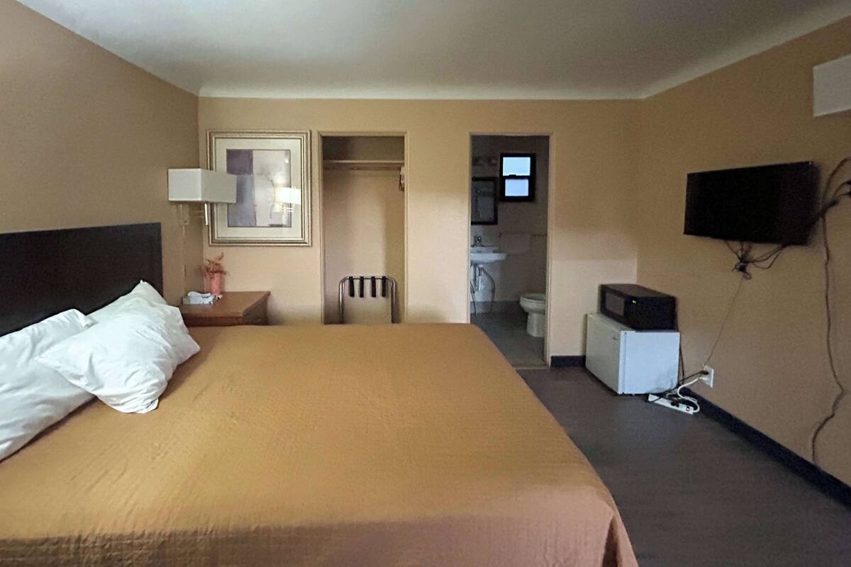 A hotel room with a bed, a nightstand, a TV, and a small kitchenette.