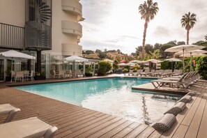 A pool area with lounge chairs and umbrellas, surrounded by palm trees and a building with a spiral staircase. - ALEGRIA Fenals Mar (Lloret de Mar)