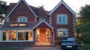 A two-story house with a brick exterior, a front porch, and a car parked in front. - Manston Guest House (Sturminster Newton)