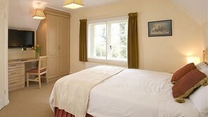 A bedroom with a bed, a desk, a chair, a television, and a window with curtains. - Manston Guest House (Sturminster Newton)