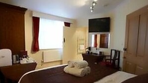 A hotel room with a large bed, a desk with a chair, a TV mounted on the wall, and a window with curtains. - Manston Guest House (Sturminster Newton)