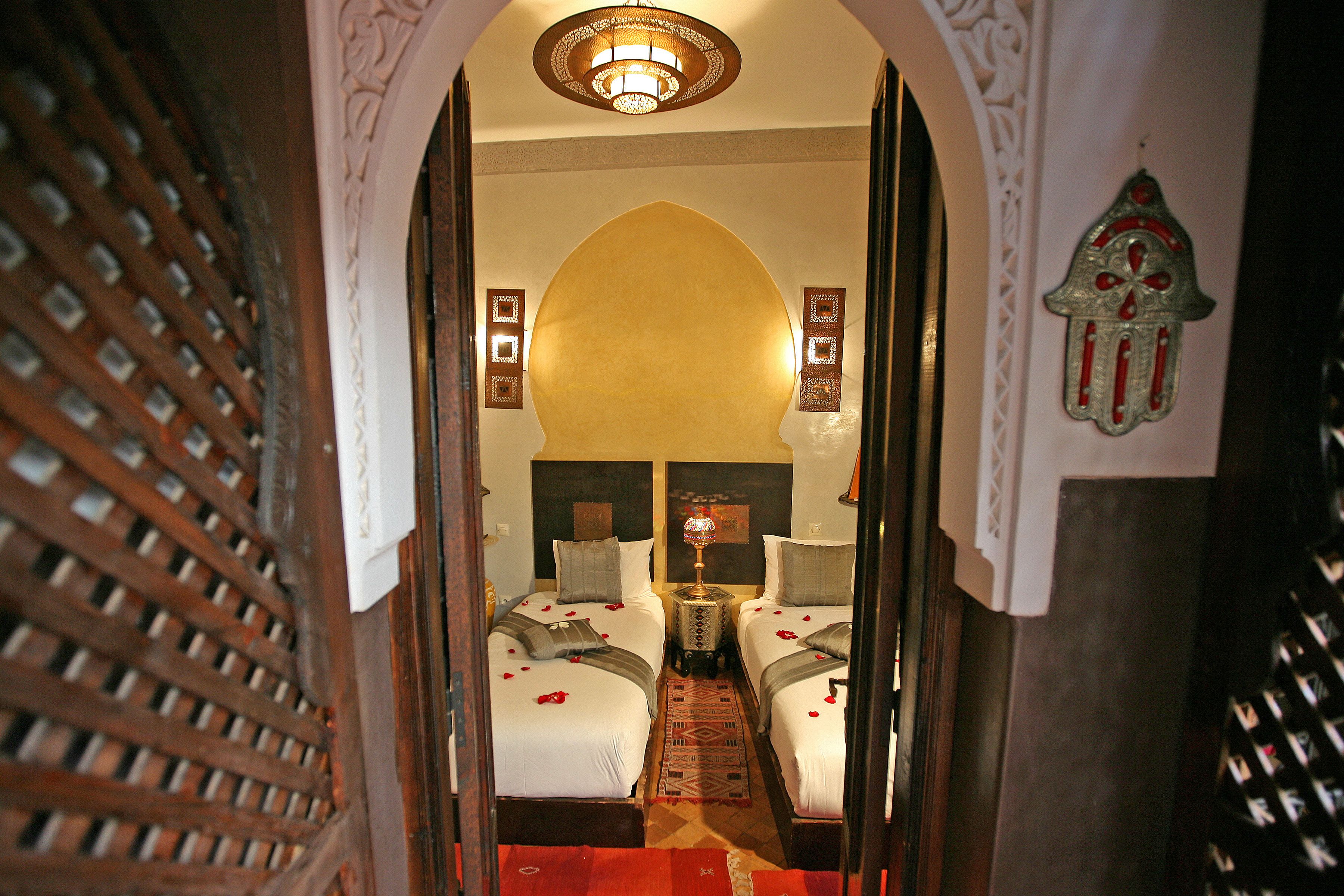 A room with two beds, a decorative rug, and a chandelier.