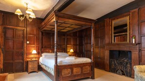A four-poster bed with a wooden frame and a mirror above it. There is a fireplace with a mantel and a mirror above it. - The New Inn by Roomsbooked (Gloucester)
