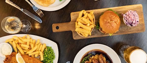 A table with various dishes including fish and chips, a burger, and a plate of sausages.