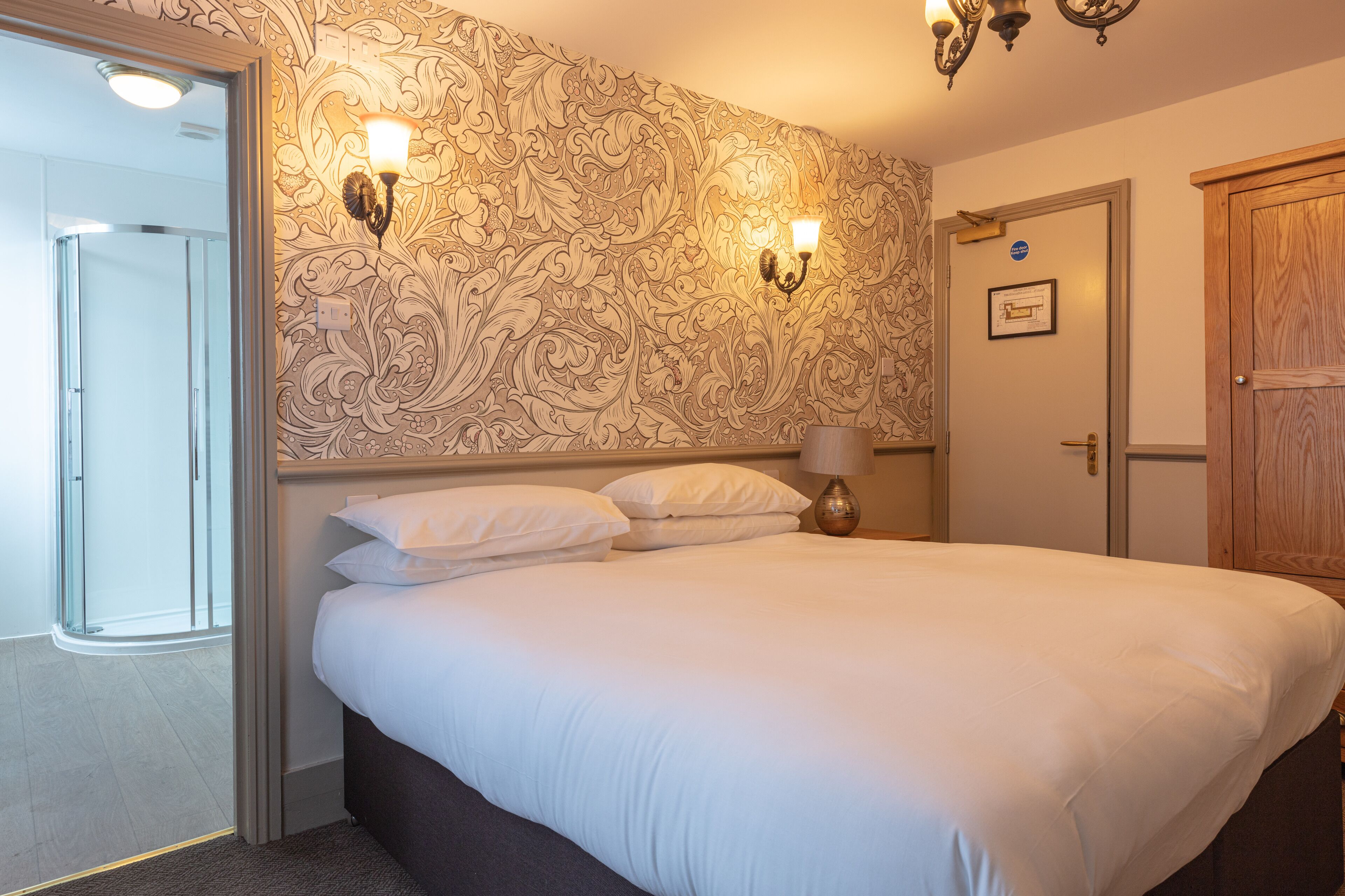 Une chambre d’hôtel avec un grand lit, deux appliques murales, une armoire en bois et une porte avec une pancarte.