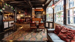 A cozy pub with wooden beams, a patterned carpet, and a sofa with red cushions. - The New Inn by Roomsbooked (Gloucester)