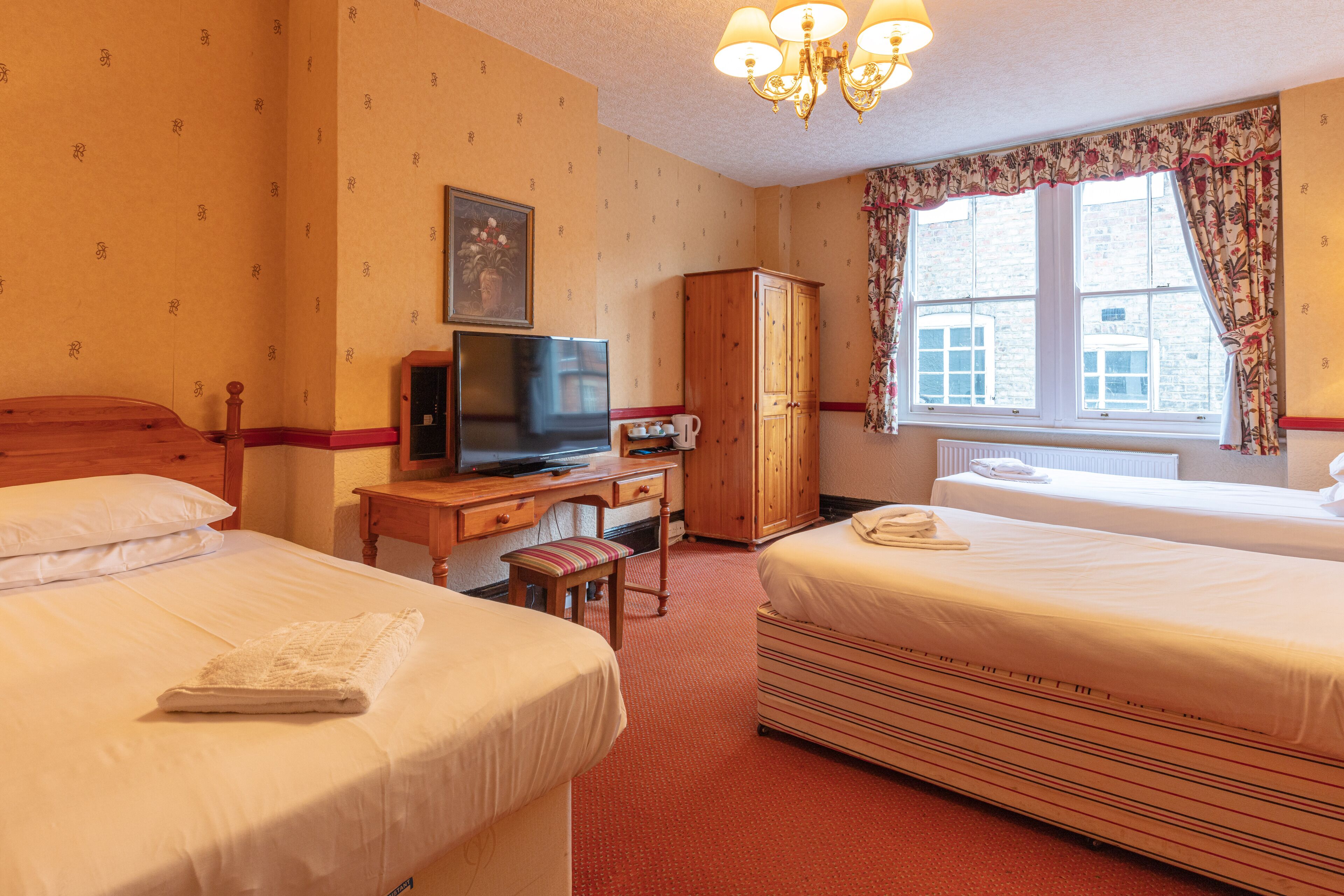 Habitación de hotel con dos camas, televisión, escritorio con silla, armario y ventana con cortinas.