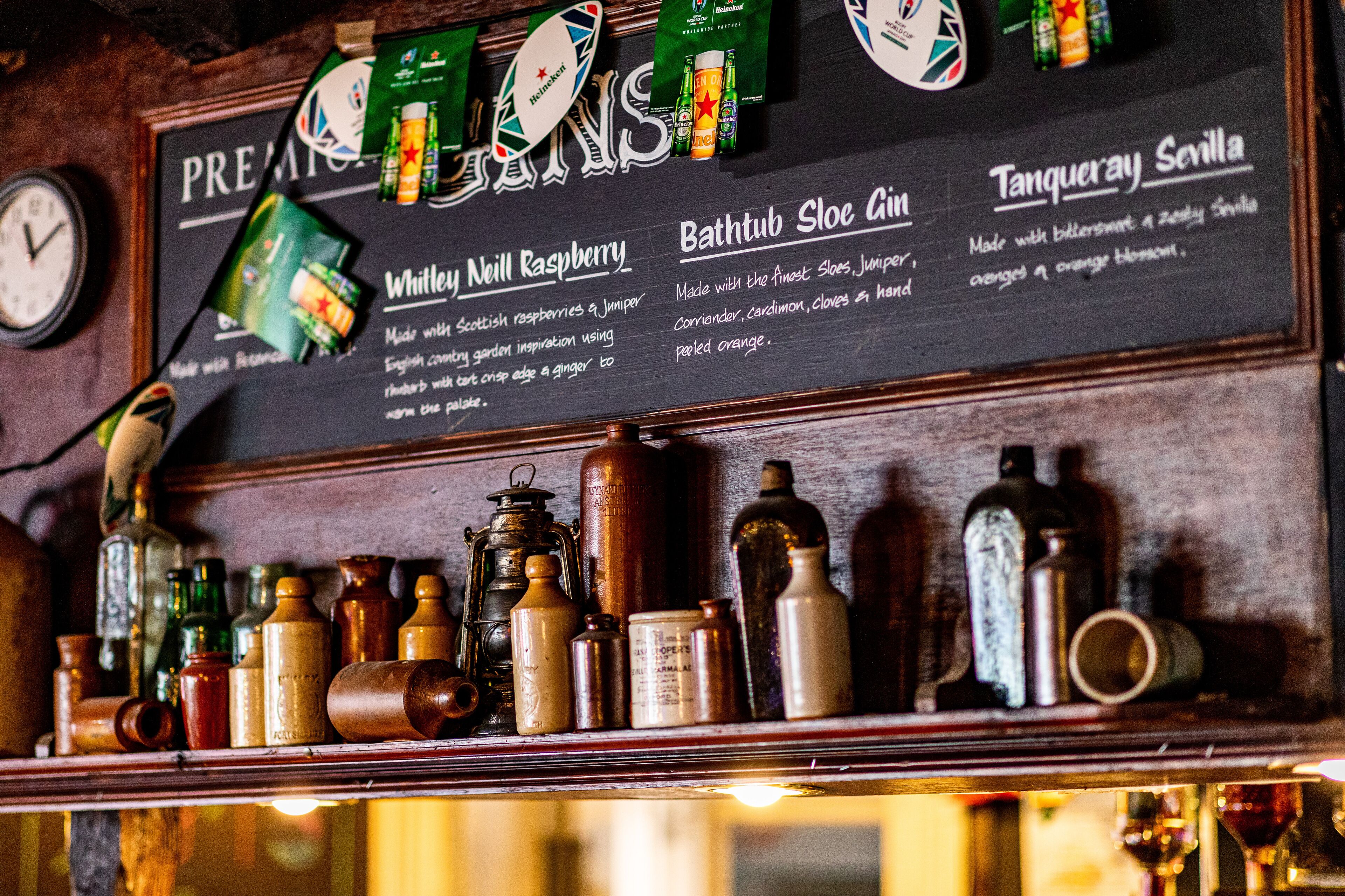 A bar menu with drink options and a shelf with various bottles and containers.