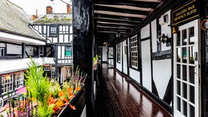 A narrow corridor with black and white timber framing, a wooden floor, and a sign indicating a gallery bar and regency suite. - The New Inn by Roomsbooked (Gloucester)