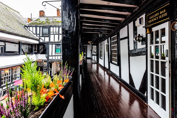 A narrow corridor with black and white timber framing, a wooden floor, and a sign indicating a gallery bar and regency suite.